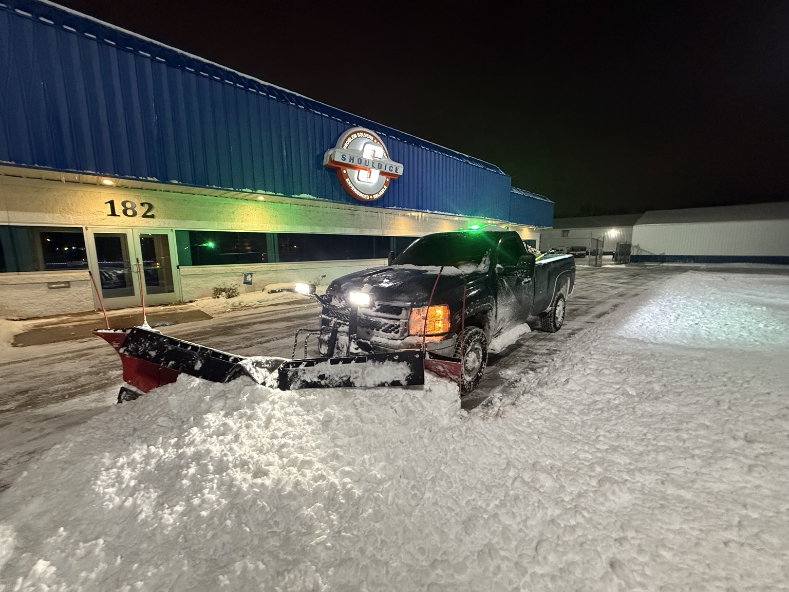 Snowplow truck clearing snow from a commercial parking lot at night