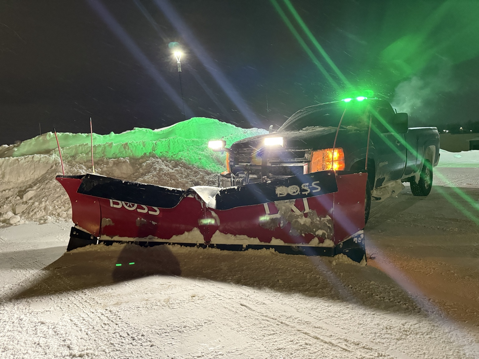 Snowplow truck working beside a large snow pile during a winter storm
