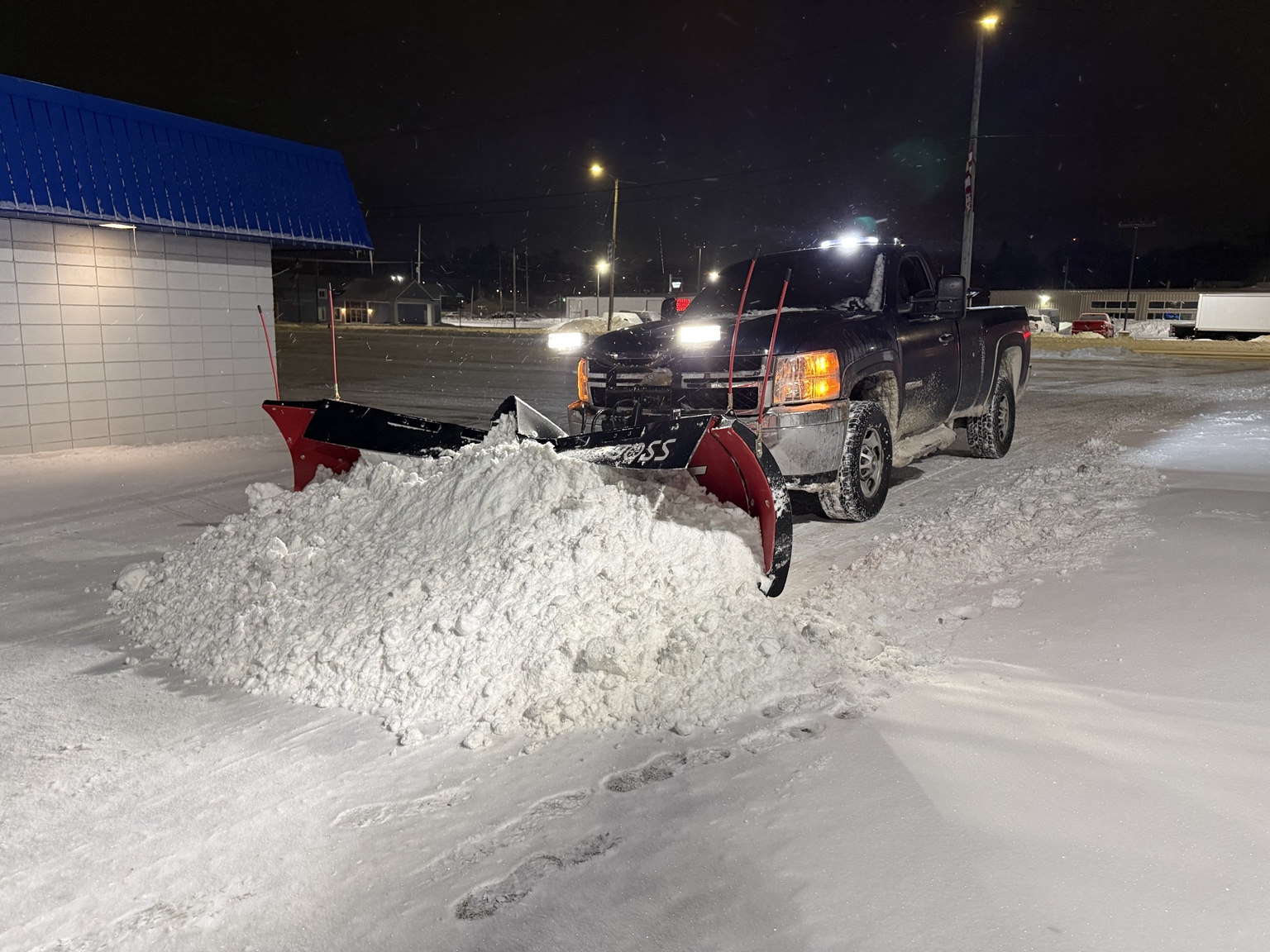 Truck pushing a large pile of snow across a commercial parking lot